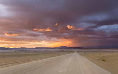 Fototapeta na wymiar Gravel road through the desert at sunset