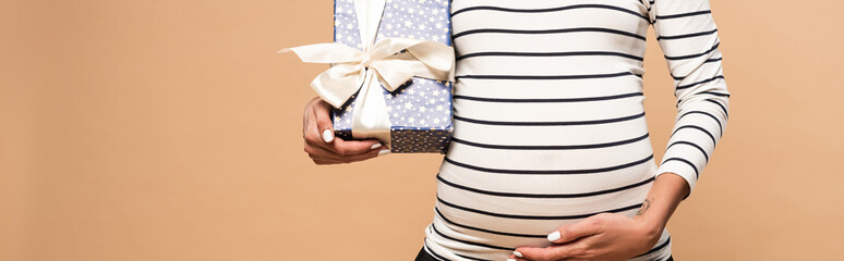 cropped view of pregnant woman holding gift on beige background