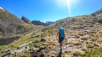 A young woman with a big backpack hikes down on a steep pathway between tall mountain peaks. Some...