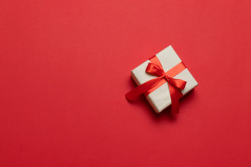 Gift or present box with red ribbon bow on red table top view. Trendy composition for birthday, mother day or wedding.