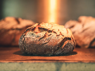 details of wholemeal rye loaf in an old oven with two blurred loaves in the background