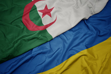 waving colorful flag of ukraine and national flag of algeria.
