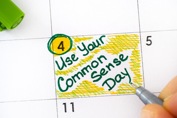 Woman fingers with green pen writing reminder Use Your Common Sense Day in calendar.