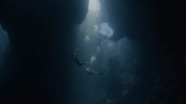 SCUBA Divers explore dark underwater cavern with light shafts