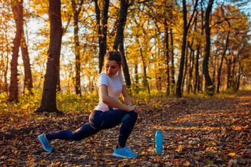 Training and exercising in autumn park. Young woman stretching legs outdoors. Active healthy...