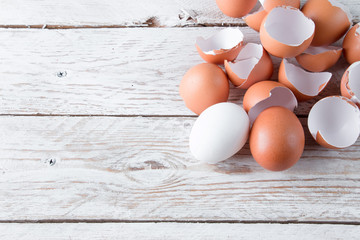 Raw chicken eggs in white and brown. Egg shells on a light wooden background.