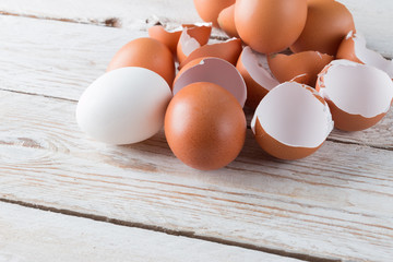 Raw chicken eggs in white and brown. Egg shells on a light wooden background.
