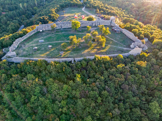 A medieval fortress with preserved walls and watchtowers on top of a high hill. The walls of the...