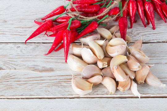Slices of fresh garlic and red hot chili peppers on a white wooden table. Seasoning for food.