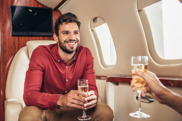 smiling boyfriend and girlfriend holding champagne glasses in private plane