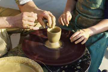 The hands of an adult man help the child to make a jug from a piece of clay on a Potters wheel