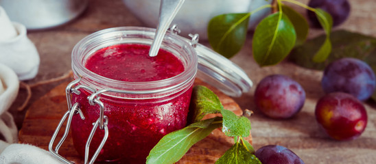 jam from fruit red plum in a glass jar and berries in a bowl on a table with copy space