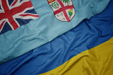 waving colorful flag of ukraine and national flag of Fiji .