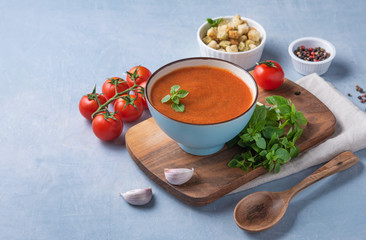 Tomato creme soup with crumbs and basil on blue background. Close up