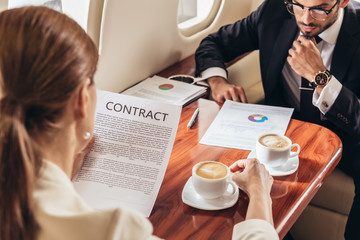 selective focus of businessman looking at document and businesswoman looking at contract in private plane
