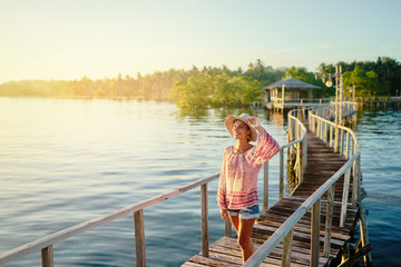 Fototapeta na wymiar Vacation on tropical island. Young woman in hat enjoying sunset sea view from wooden bridge terrace, Siargao Philippines.