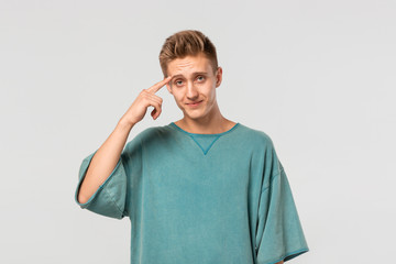 Thoughtful young man in a green tee holds finger close his head isolated over white background.