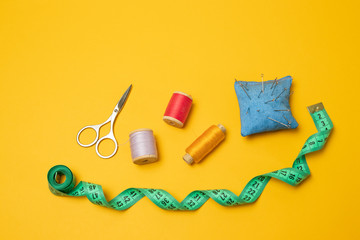 Composition with threads and sewing accessories on a yellow background. Top view, flat lay. Copy space for text.