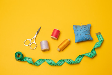 Composition with threads and sewing accessories on a yellow background. Top view, flat lay. Copy...