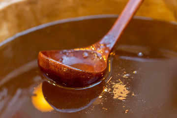 Wooden spoon in a barrel with honey, closeup. Amber transparent fresh honey in a large can