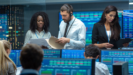 Multi-Ethnic Team of Traders is Busy Working at the Stock Exchange Office. Dealers and Brokers Buy and Sell Stocks on the Market. Monitors Display Relevant Infographics, Data and Numbers.