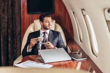handsome businessman in suit holding cup of coffee in private plane