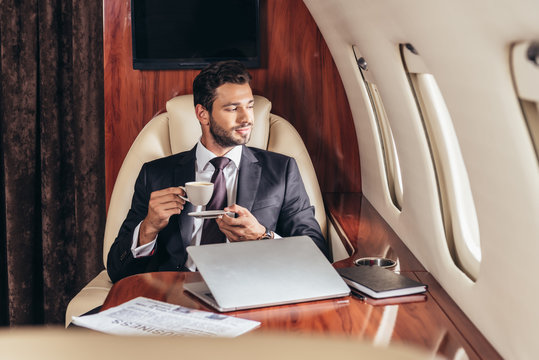 handsome businessman in suit holding cup of coffee in private plane