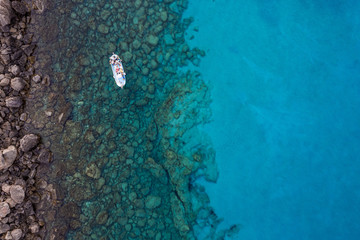 An aerial view of a boat the beautiful Mediterranean sea, where you can se the rocky textured underwater corals and the clean turquoise water of blue lagoon Agia Napa