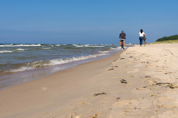 Couple walking on a sandy seashore on a sunny summer day. Wild beach, vacation and sports activities with a bicycle. 