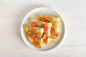 Crepes with strawberry and honey on white plate