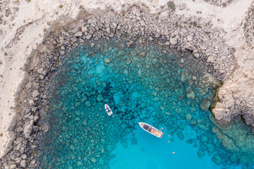 An aerial view of a boat the beautiful Mediterranean sea, where you can se the rocky textured underwater corals and the clean turquoise water of blue lagoon Agia Napa