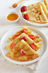 Crepes with strawberry and honey on white plate