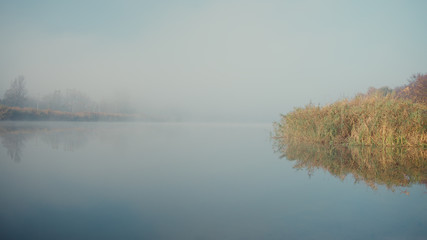 Dawn fog over the river. The reeds are reflected in the water.