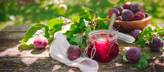 Glass jar with plum jam confiture and ripe plum berries in a basket on a wooden vintage table in...