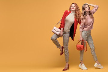 Fototapeta premium Fashionable autumn woman with stylish hairstyle, makeup dance. Two Shapely blonde redhead girl having fun, trendy red pink outfit, fashion hair. Gorgeous female model, beauty style concept