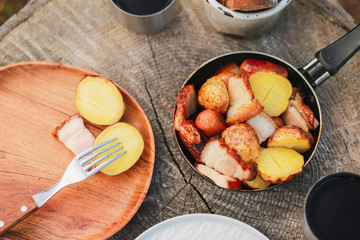 Roasted potatoes in rind with bacon, meat. Fried potatoes in a frying pan in the woods. Bread fried on a fire. Camping with food. Picnic on a stump with tea. Fried sausages. To eat in nature