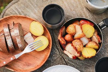 Roasted potatoes in rind with bacon, meat. Fried potatoes in a frying pan in the woods. Bread fried on a fire. Camping with food. Picnic on a stump with tea. Fried sausages. To eat in nature