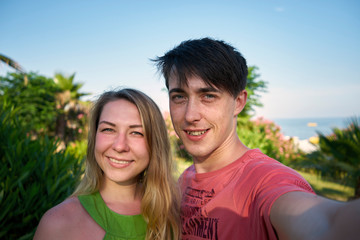 Fototapeta premium man and woman take a selfie on a background of palm trees and greenery