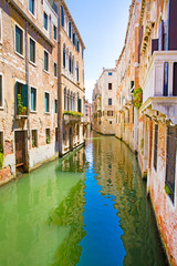Narrow canal in Venice, Italy. Old historical buildings and bright green water. Vacations in Italy. 