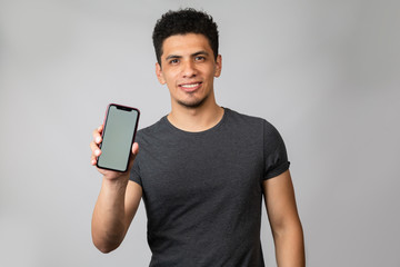 Smiling latin man showing cellphone screen - man in studio with gray background