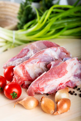 Raw meat slices on chopping board with fresh vegetables and spices