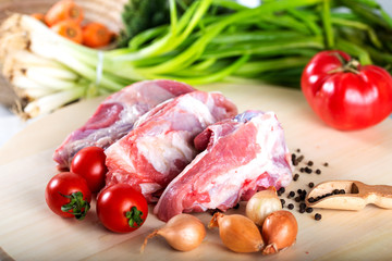 Raw meat slices on chopping board with fresh vegetables and spices