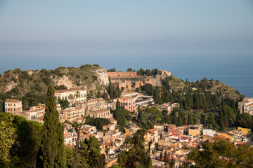 Fototapeta na wymiar Beautiful panorama from mountain top to a small mediterranean sicilian town, Taormina, in warm sunset with the sea in the background, Sicily, Italy 