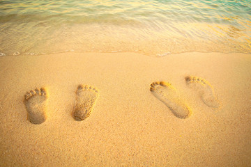 Feet prints on the sand of the beach with sea wave. Top view. Two people foot marks on sand.