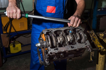 A mechanic with a wrench disassembles a car engine. Work in the garage.