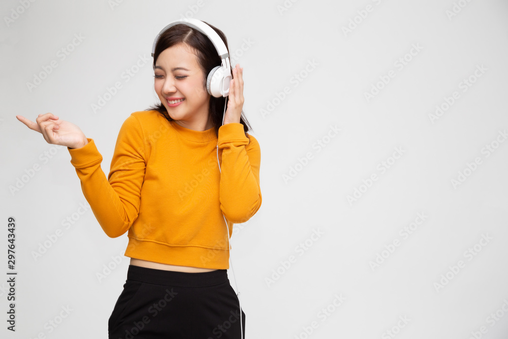 Wall mural beautiful young asian woman with headphones listening to music in bright outfit enjoying the song me