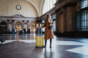 Tourist woman with suitcase retro camera on platform station in Barcelona. Girl traveler waiting...