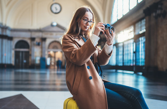 Tourist woman suitcase on platform station in Barcelona taking photo on retro camera. Girl traveler waiting train enjoy holiday weekend vacation in transport railway. Travel railroad station concept