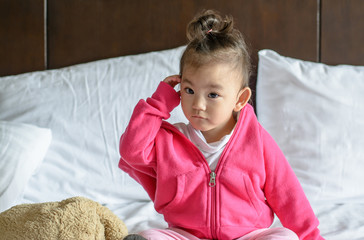 cute asian baby girl wearing a pink jacket sitting on the bed.