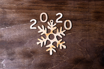 Wooden figures 2020 and snowflake on a dark wooden background. View from above